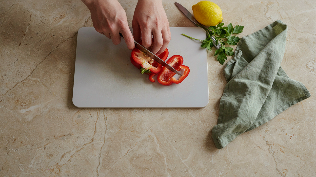 Hands slicing a red pepper on a smooth light grey cutting board