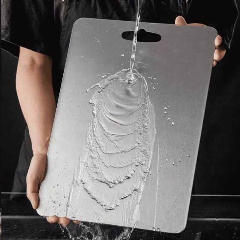 Water rinsing cleanly off a titanium cutting board held under the tap